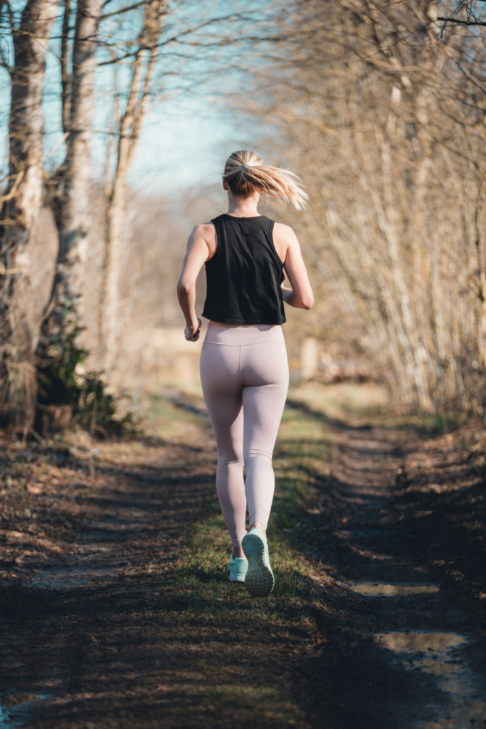 Woman running alone on a wooded trail at sunset
