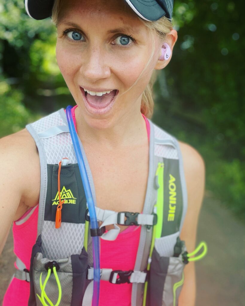 Coach Mandy smiling in a hydration vest on a trail run
